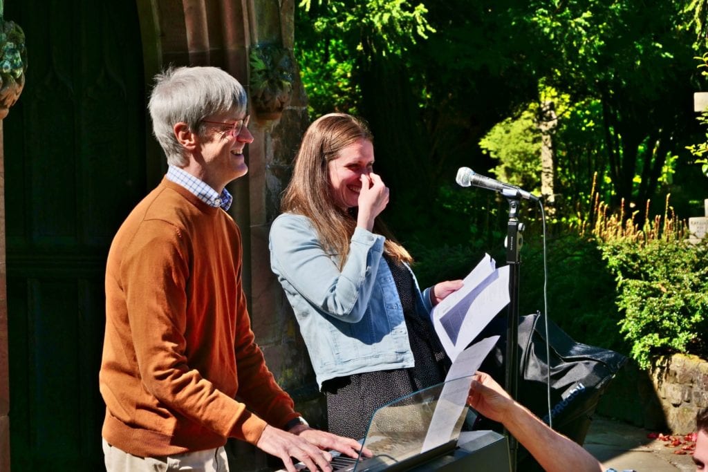 A keyboard player and a singer laughing together outdoors